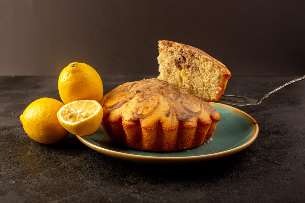 front-closed-up-view-round-sweet-cake-delicious-yummy-choco-cake-sliced-inside-blue-plate-along-with-fresh-lemons-dark