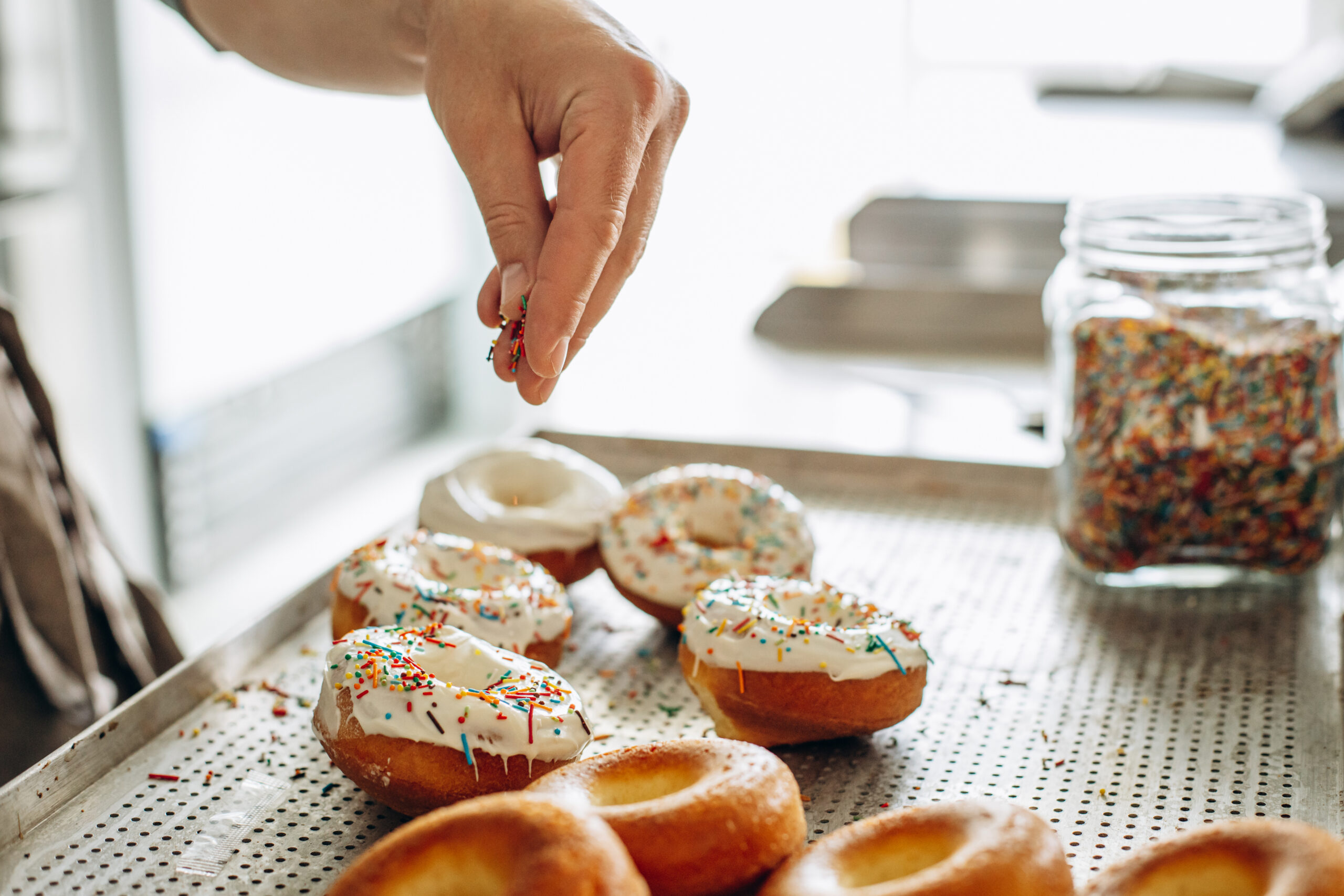 Man baker sprinkles donuts with colorful sweets