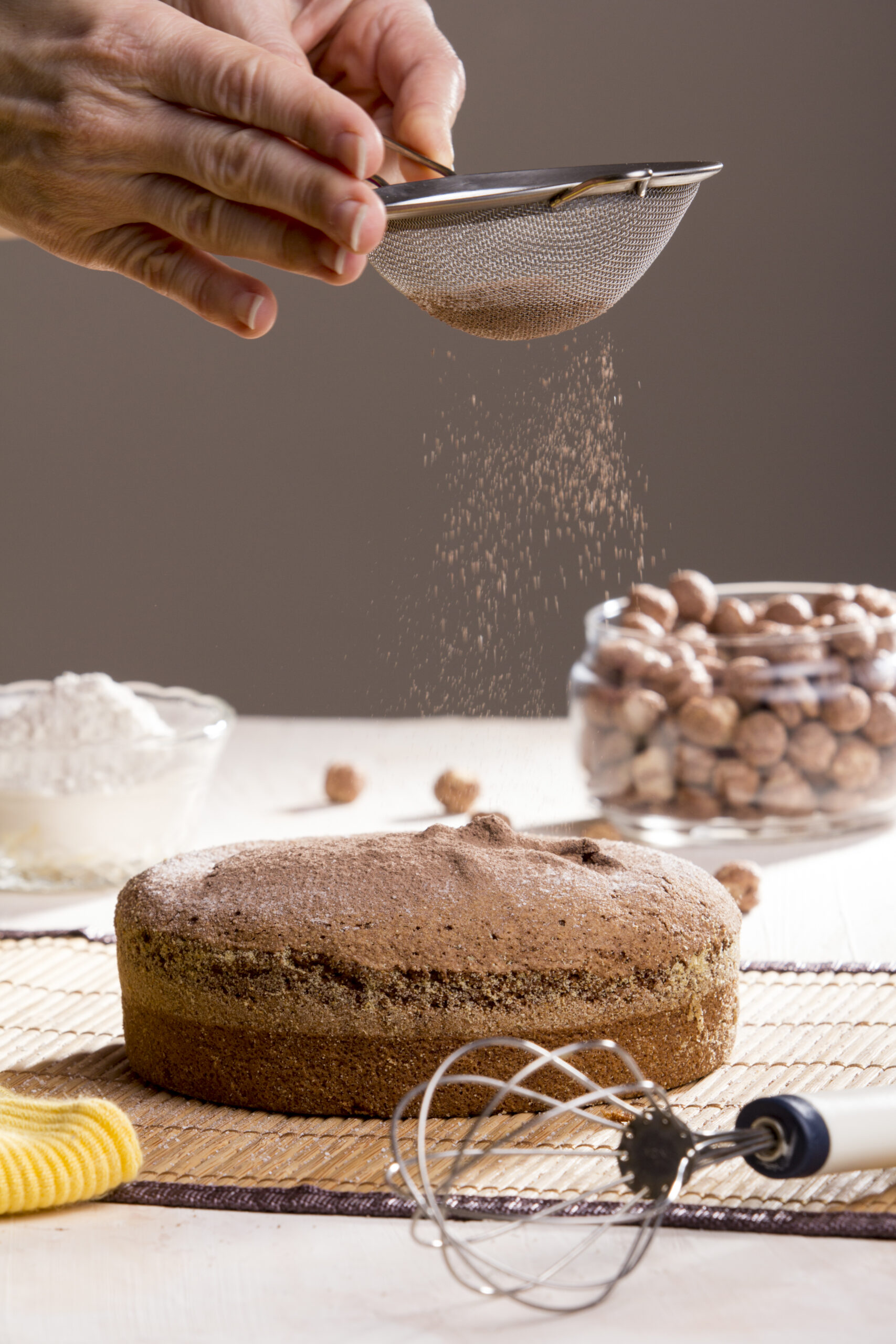 Vertical shot of a freshly baked chocolate hazelnut cake being covered in cocoa powder